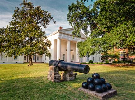 cannon and cannonballs stacked outside in lawn in front of white state house building