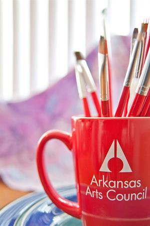 red mug with arkansas arts council logo and paintbrushes inside