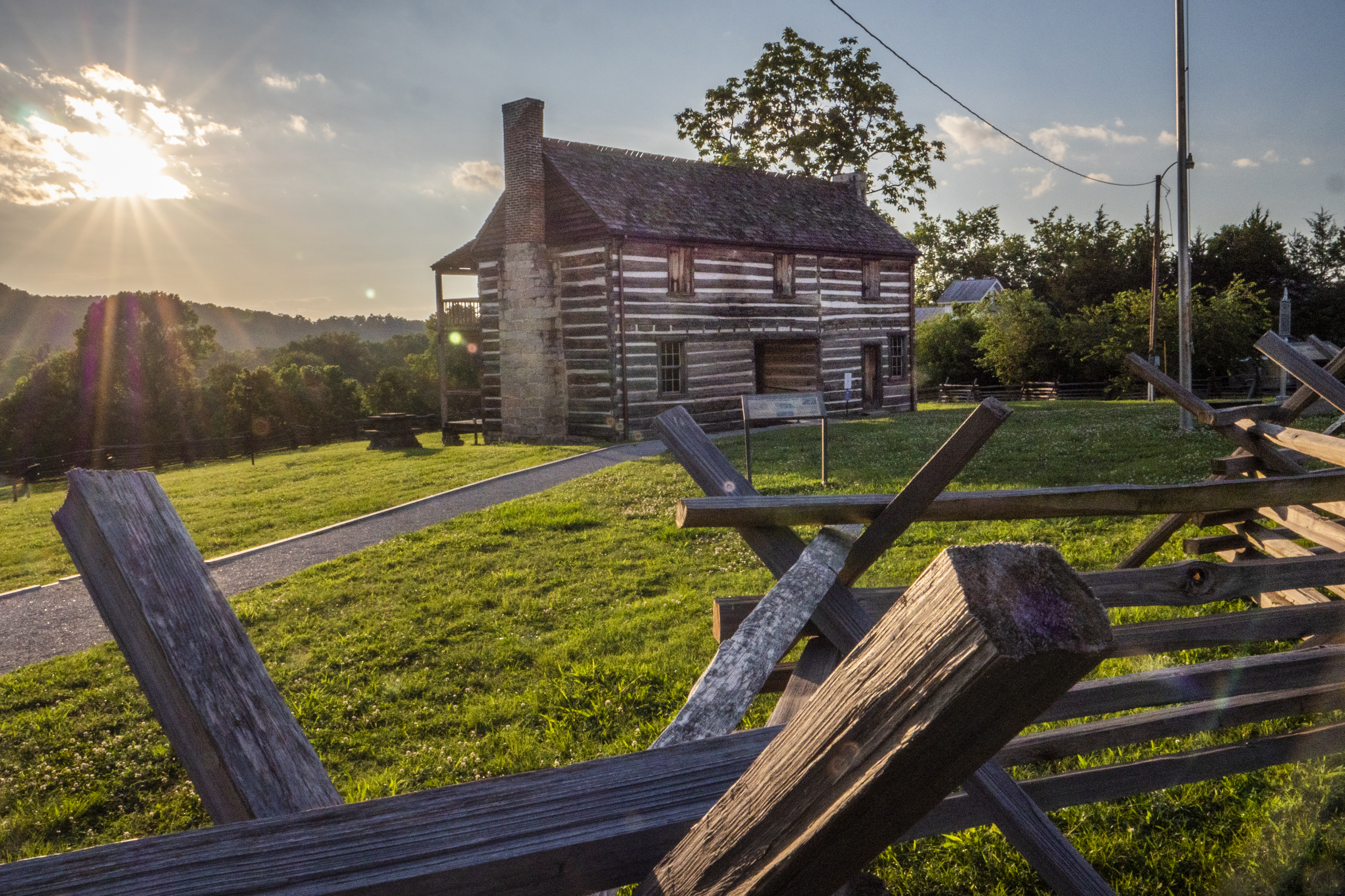 A historic two story building behind a wooden split-rail fence at sunset.