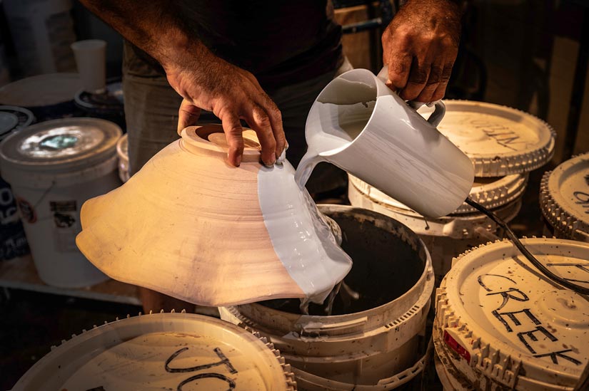 A man pouring slip over a pottery object. 
