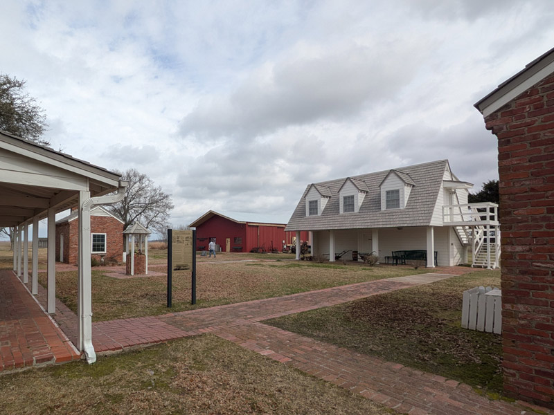 Historical buildings in a small grassy square with brick paths and an informational sign.