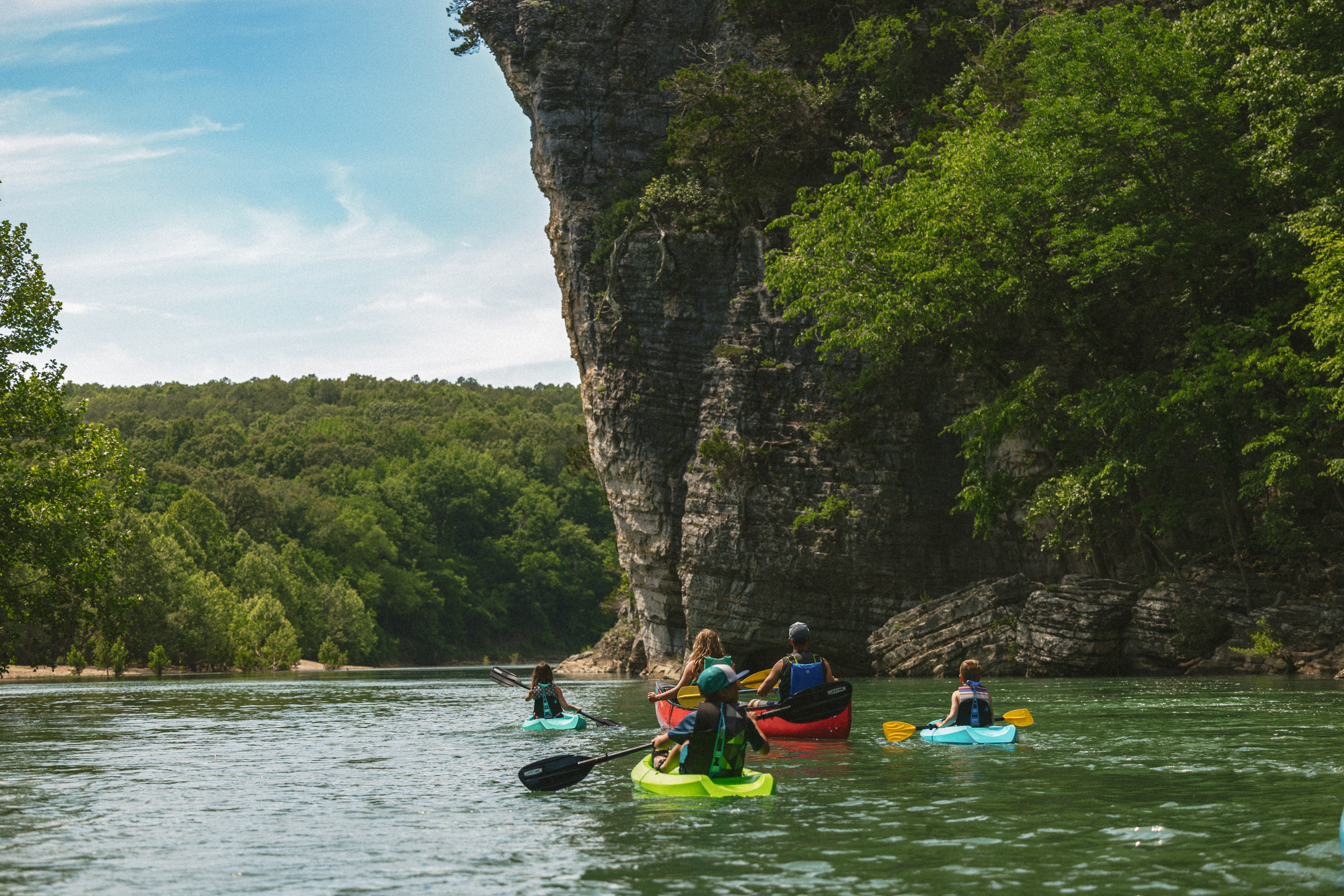 A family in kayaks and canoes floats down the Buffalo River next to a bluff.
