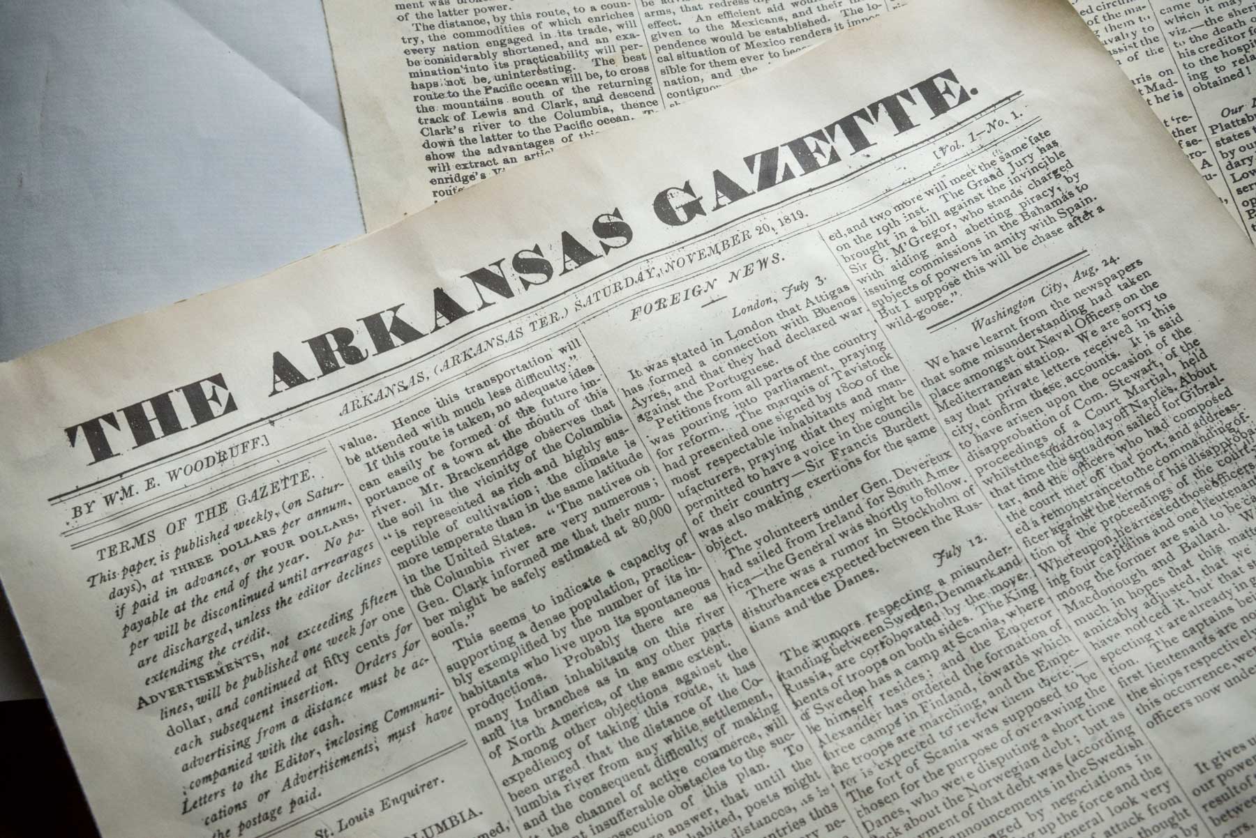 A closeup of The Arkansas Gazette newspaper sitting amongst other papers. Issue from 1819