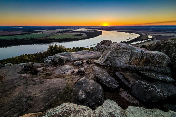 View of large boulders in the foreground and a long river in the background from Scouts Point at sunrise.