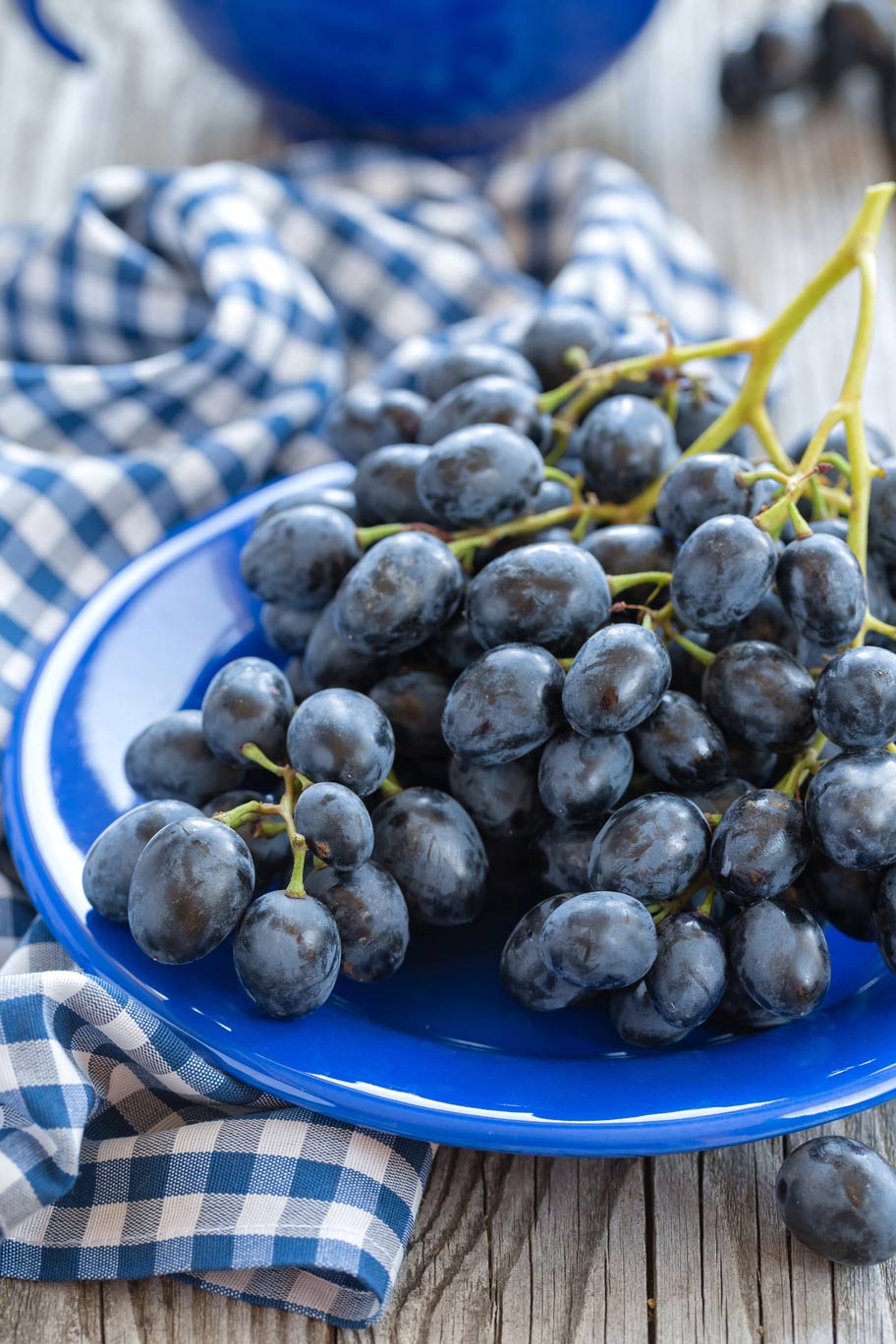 A bundle of bluish purple cynthia grapes sitting on a blue plate