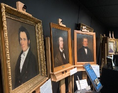 ASA_Exhibit_Brushed_into_History Old framed paintings of men in suits displayed side by side on easels.