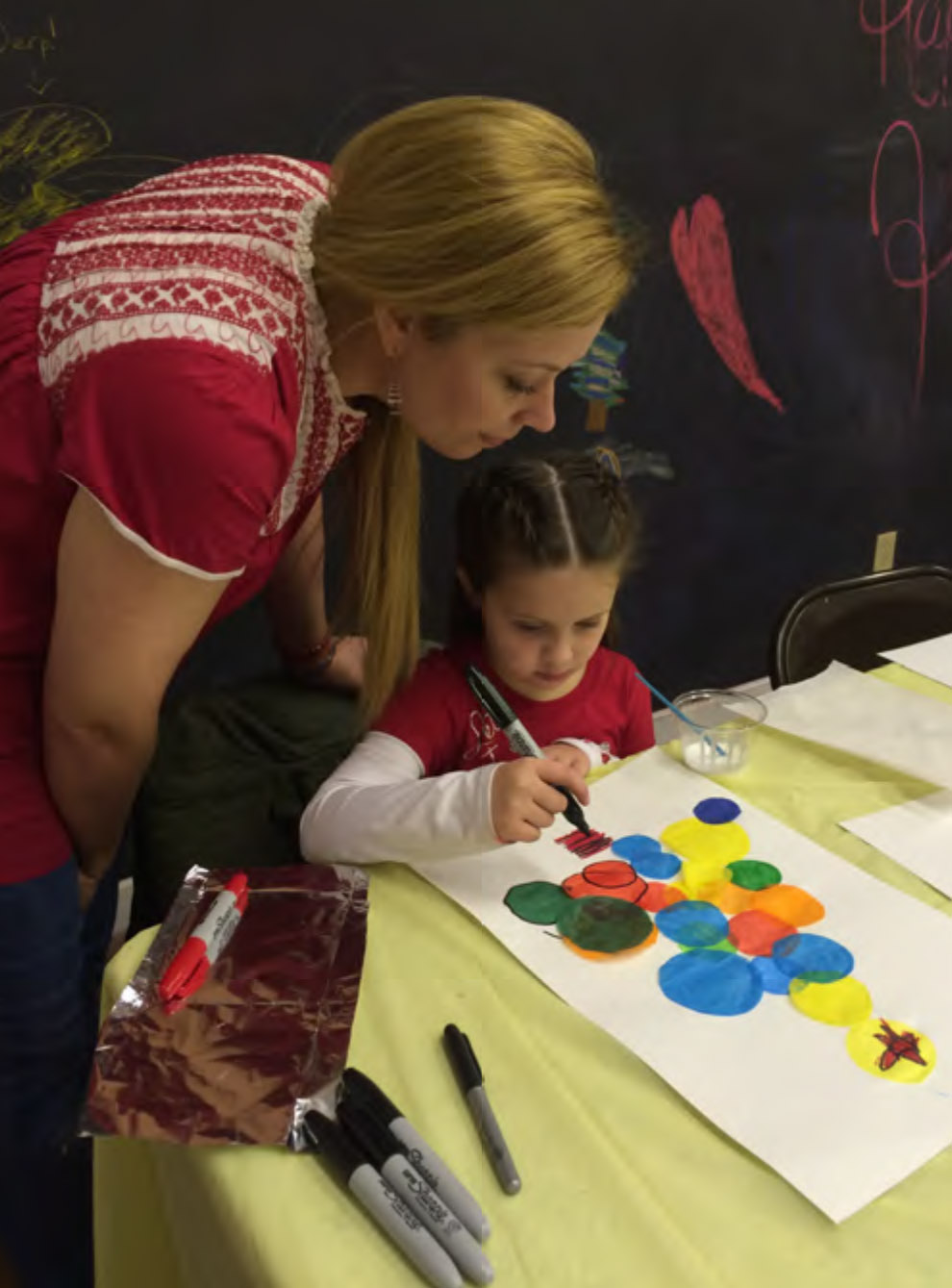 woman standing over young girl who is painting