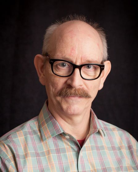 headshot of man in glasses with mustache wearing plaid shirt