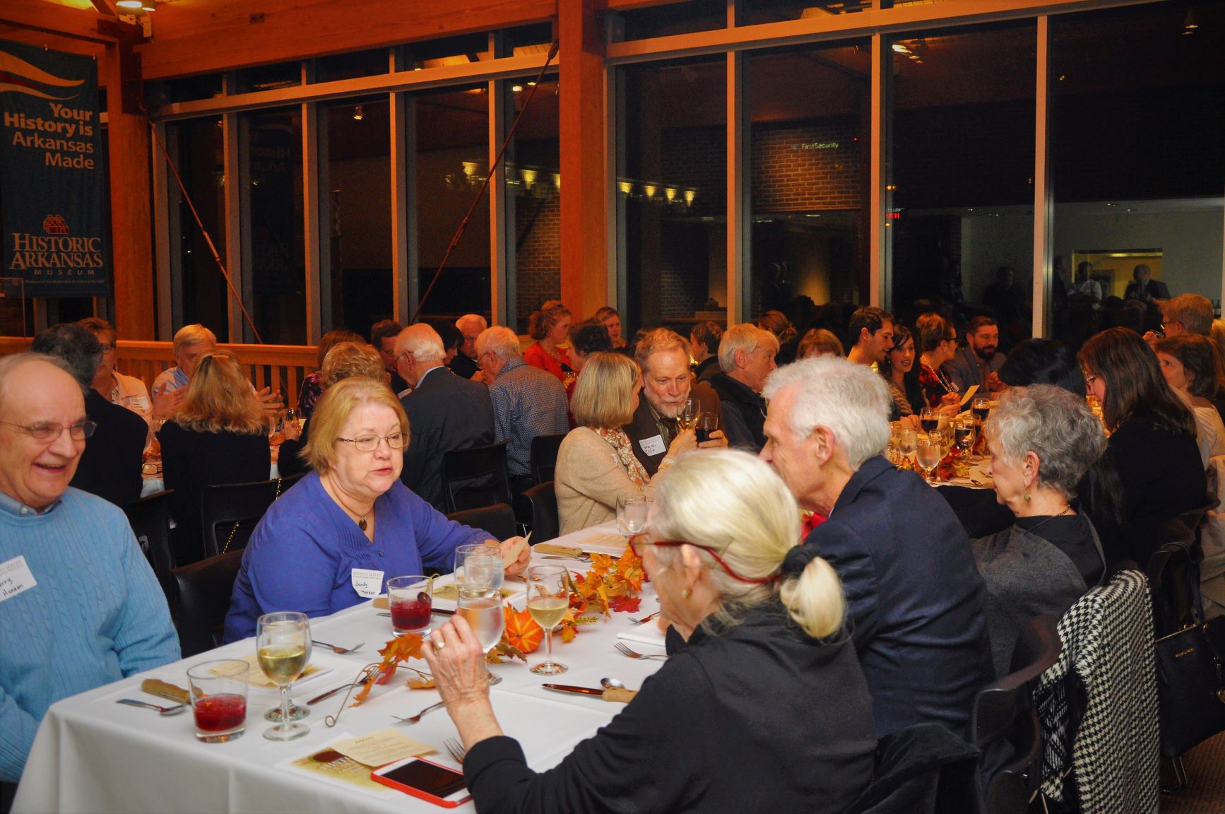 people sitting at rectangular tables with tablecloths eating food and drinking