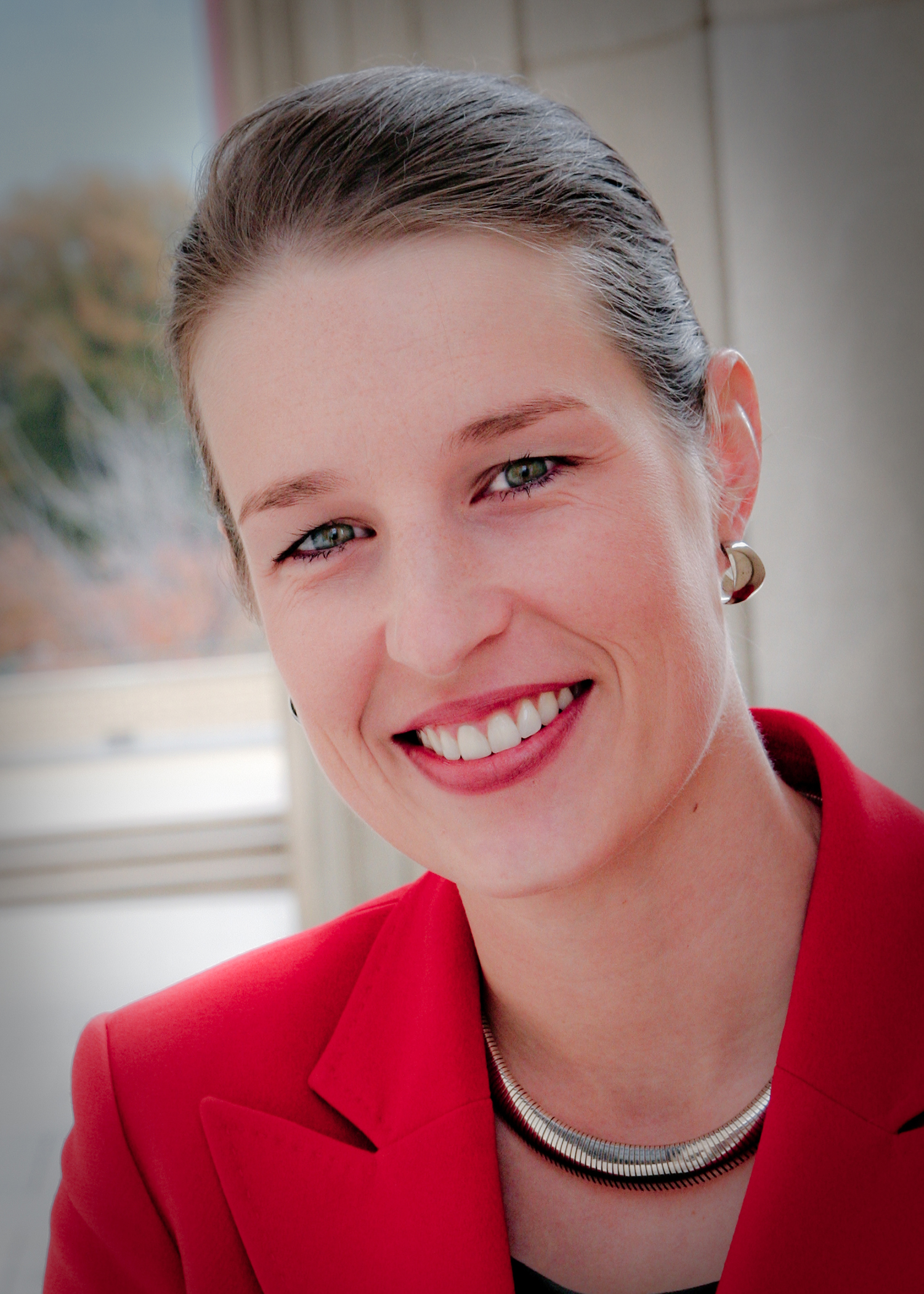 profile view of smiling woman in red suit jacket wearing jewelry