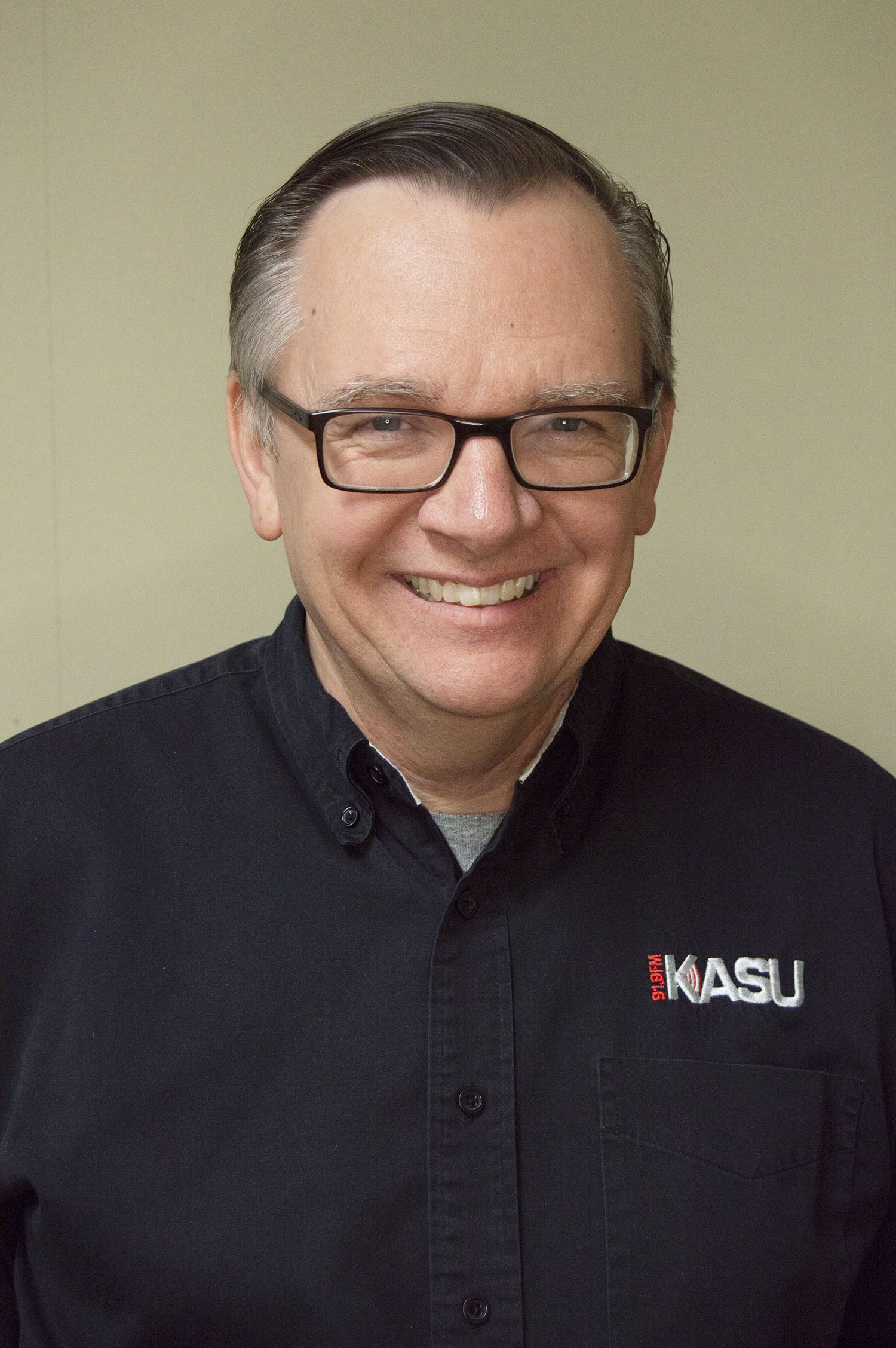 headshot of smiling man wearing glasses and dark shirt