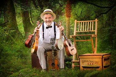 man in a hat, suspenders, and bowtie sitting and holding ukuleles and banjo