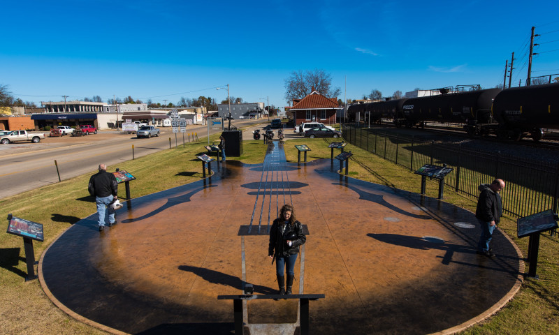 Three people standing and reading raised plaques on top of concrete shaped and painted like a guitar.