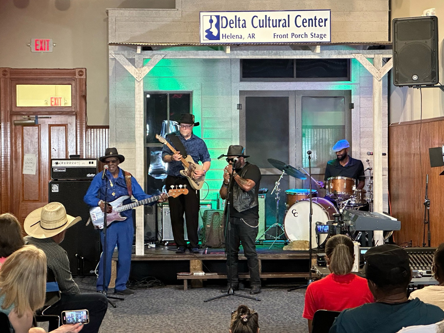 Four men playing instruments for an audience on a stage made to look like a porch.