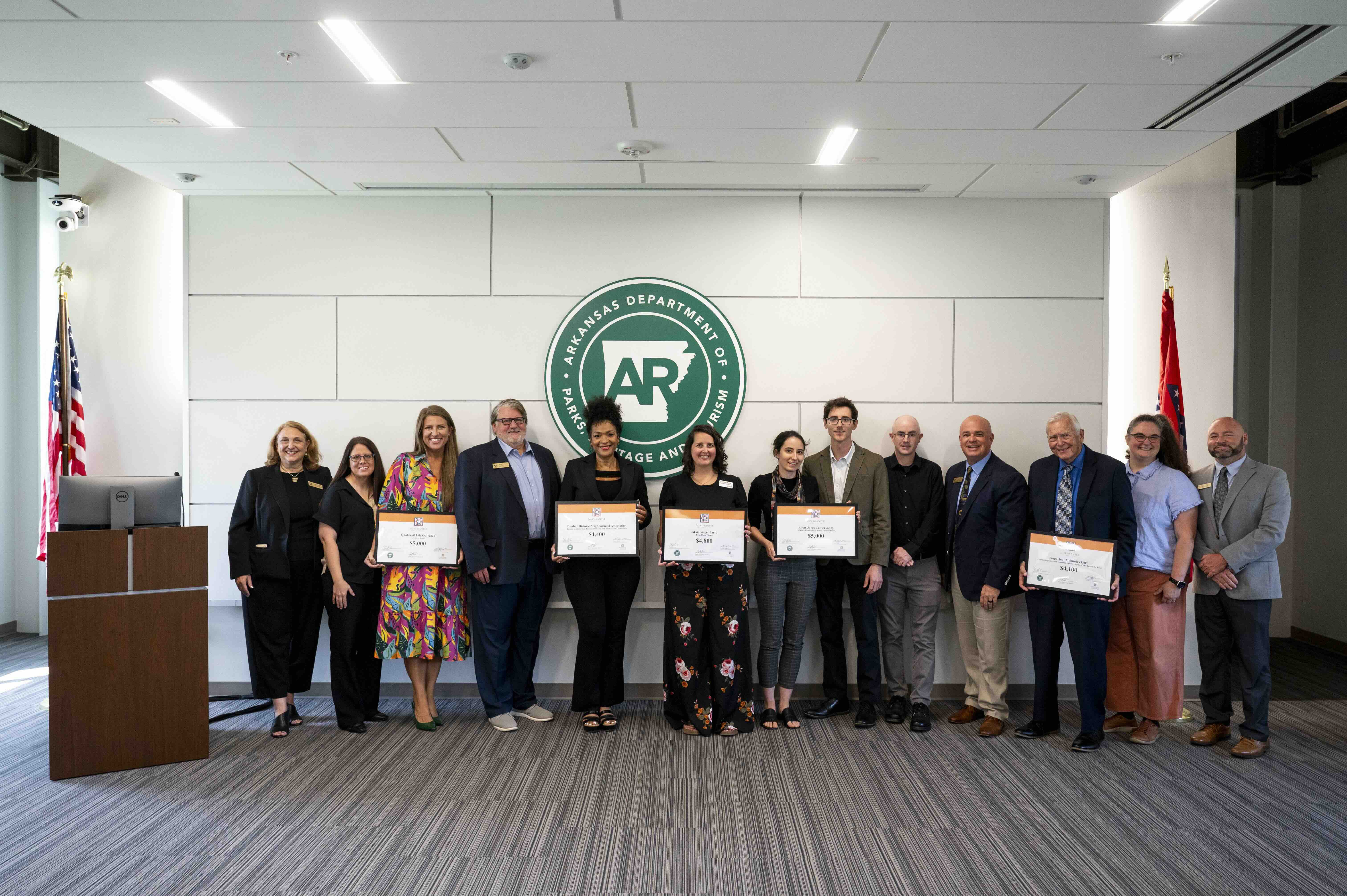 Grants2 A group of grant recipients holding framed certificates posing in front of a large white wall.