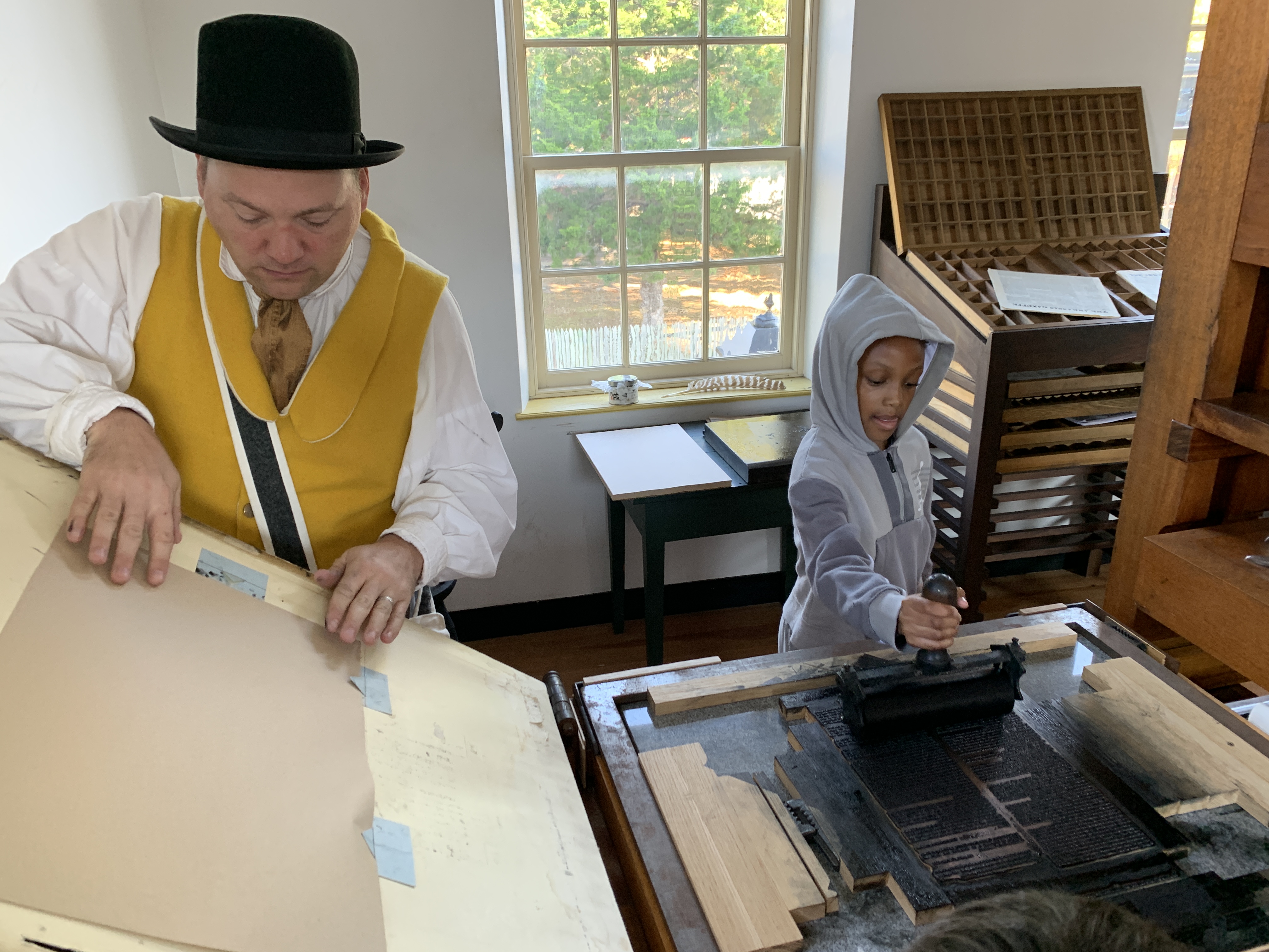 A man in period clothing teaching a child how to use the print press.