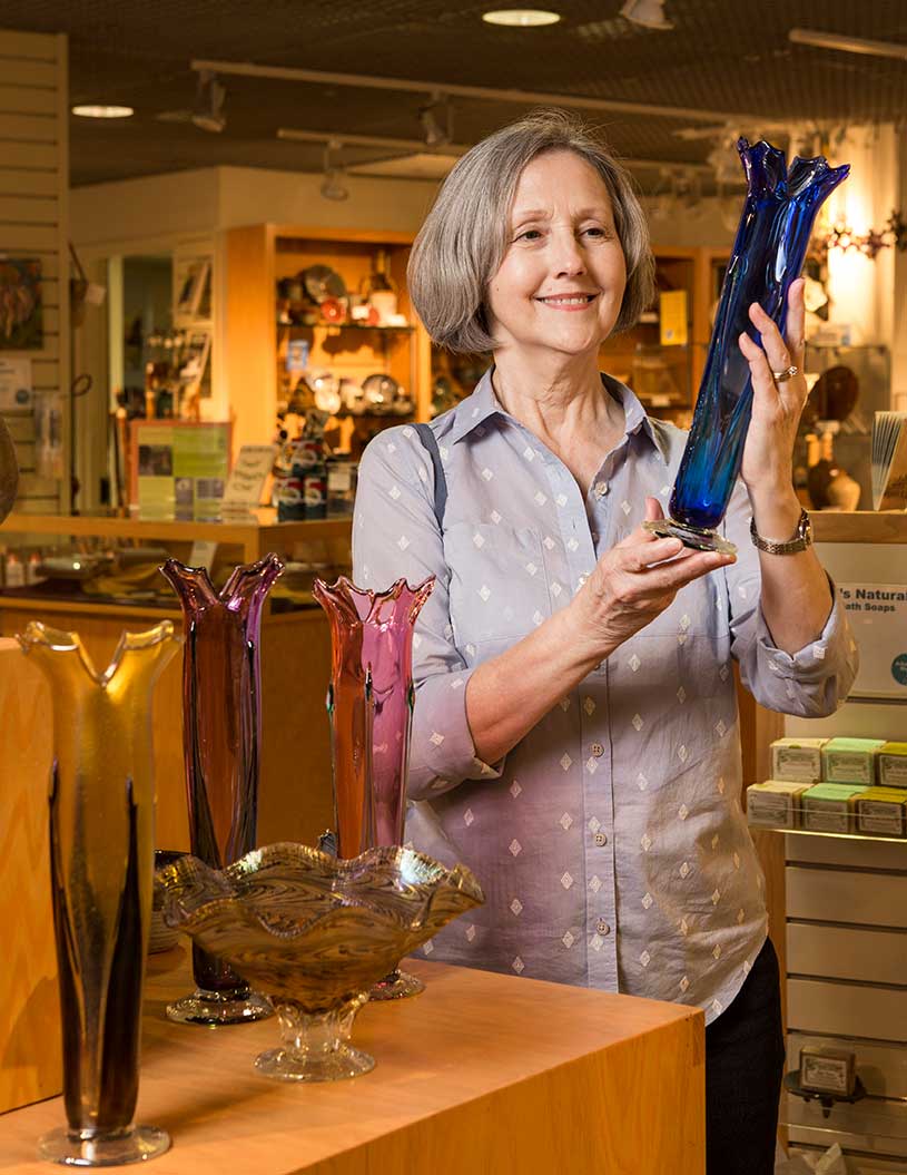 A woman holding a blue vase and smiling inside a museum store.