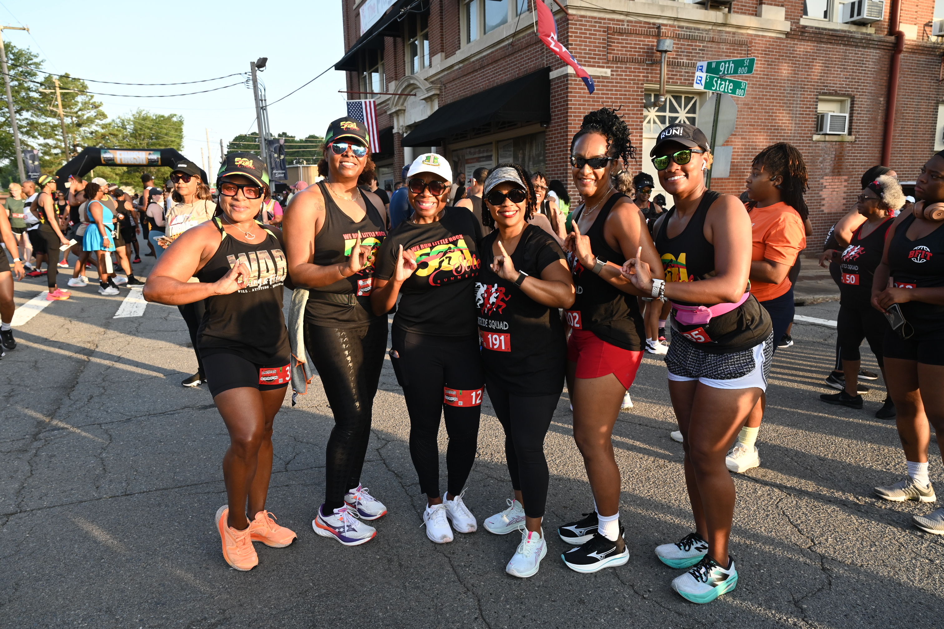 Six ladies in athletic wear pose side by side with their pinkies up.