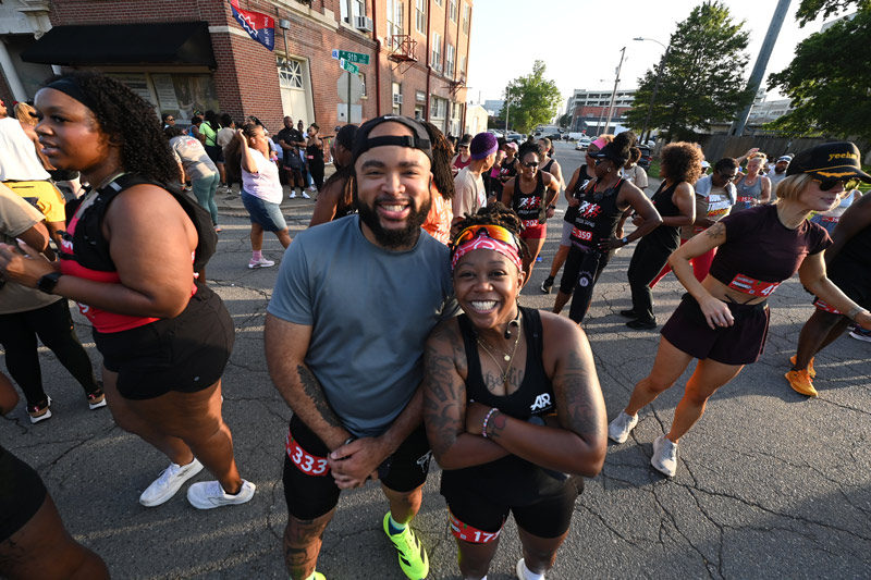 A man and a woman in athletic wear pose smiling next to one another.