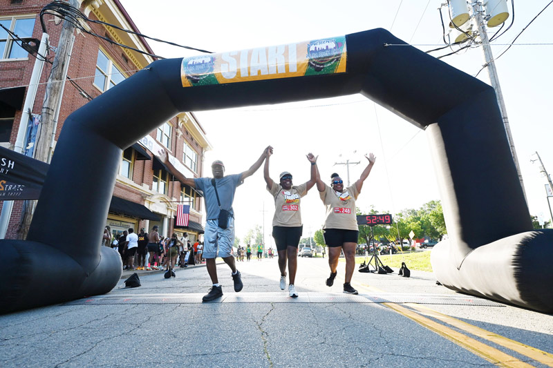 Three racing contestants raise their hands in the air as they pass the finish line.