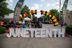 FiveladiesposetogetherbehindalargeJunteenthsignunderaballoonarch