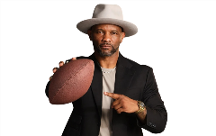 Amaninablackblazerandagrayhatholdsafootballinhisrighthandandpointstoitwithhisleft