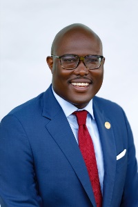 Amanwithdarkcoloredglassesinabluesuitwitharedtiesmiling
