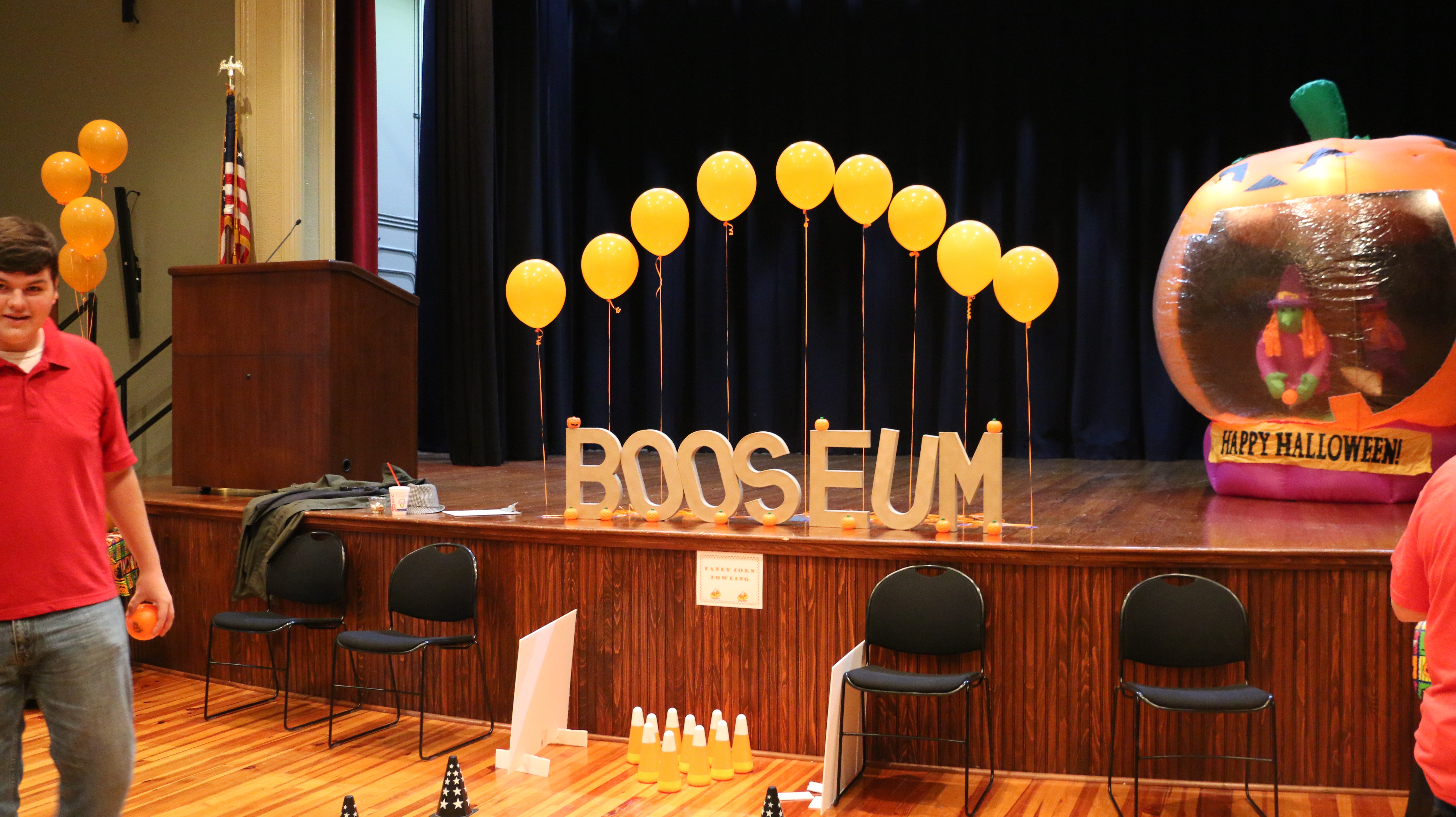 Booseumletteringstandinguponastagewithballoonsandablow-upjack-o-lantern