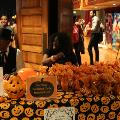 festivalentrancetablewithjack-o-lanterntableclothbucketsandpartyfavorbagsandpeoplesittingbehindit