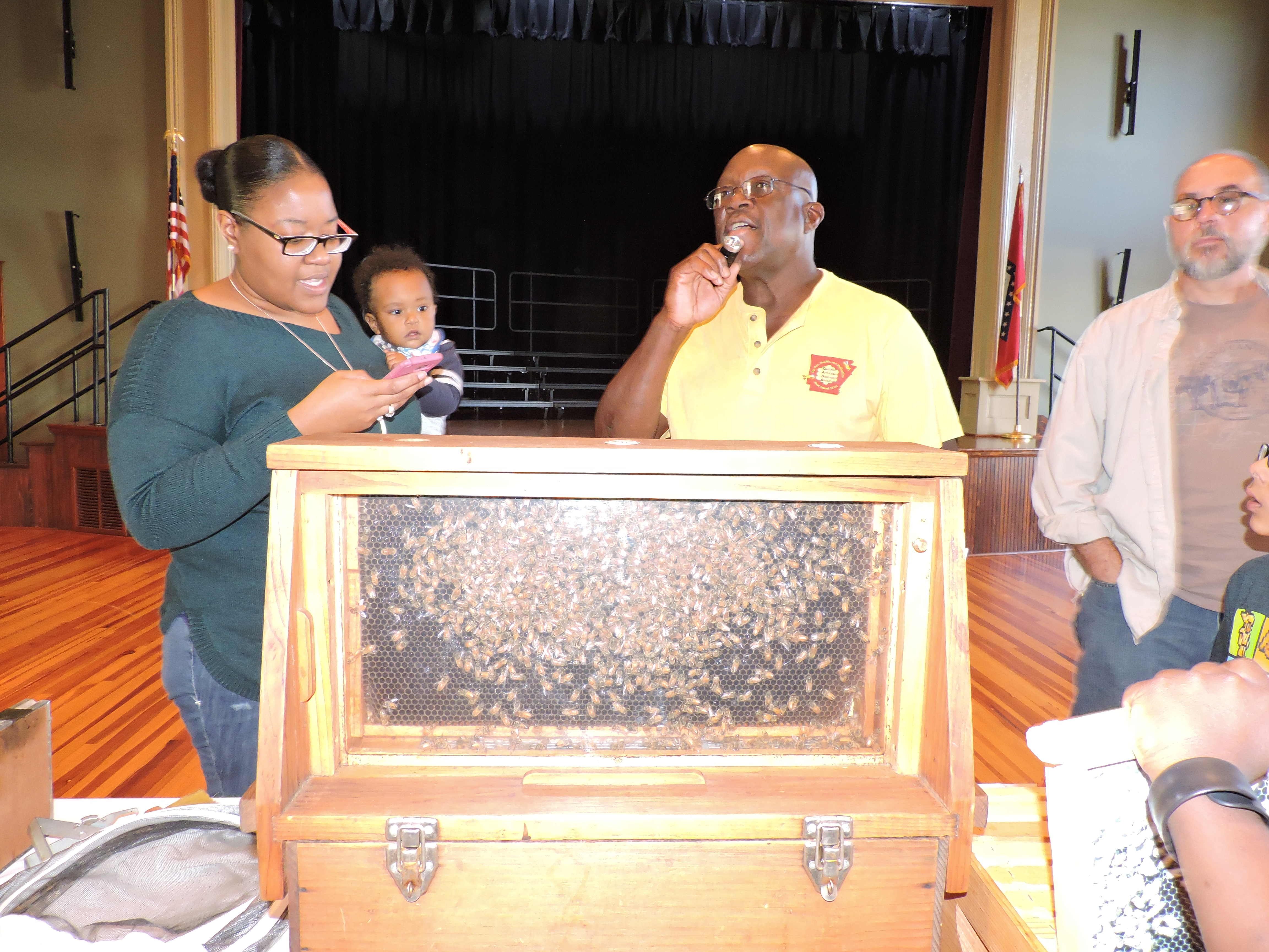 womanholdingababyandmangivingademonstrationofbeesinacaseinfrontofhim