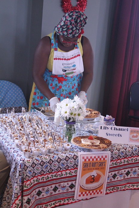 womanstandingbehindtableofcolorfulpatternedtableclothdessertsandflowersinajar