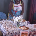 womanstandingbehindtableofcolorfulpatternedtableclothdessertsandflowersinajar