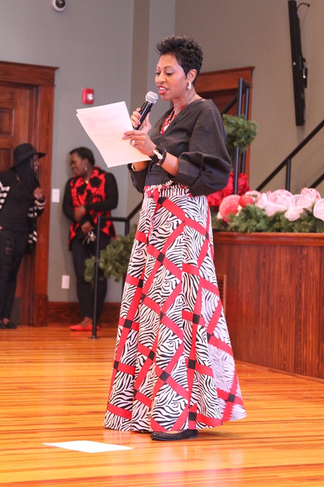 woman in red and zebra-print dress holding paper and speaking into microphone