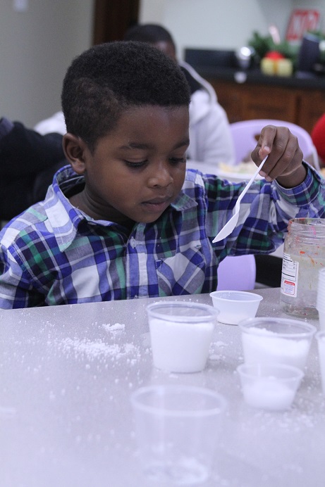 youngboyinplaidshirtholdingaspoonandlookingatplasticcupsfullofwhitecontents