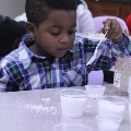 youngboyinplaidshirtholdingaspoonandlookingatplasticcupsfullofwhitecontents