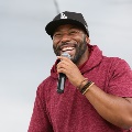 manwithmicrophonesmilingandwearingbeadedbraceletsblackbaseballcapandredshort-sleevehoodie