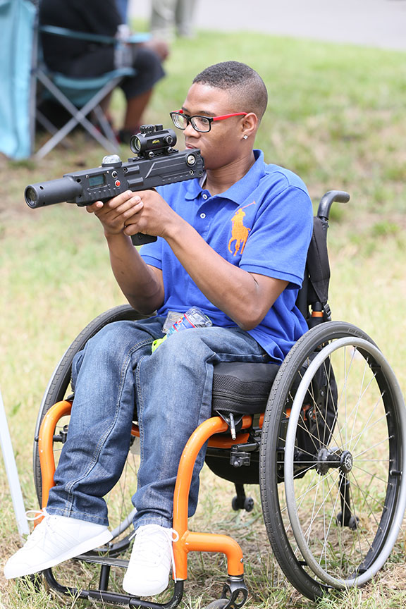 youngmanwearingglassesandbluepoloshirtinwheelchairholdinggun