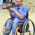 youngmanwearingglassesandbluepoloshirtinwheelchairholdinggun