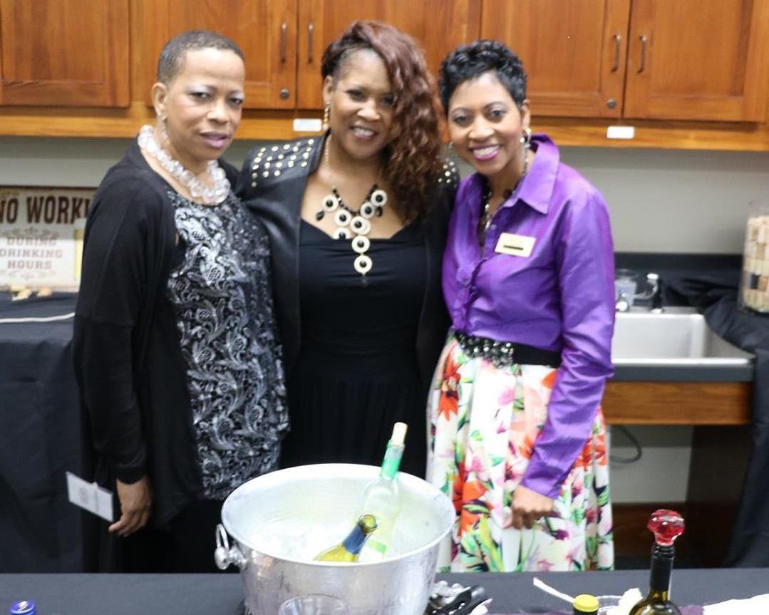 threewomeninkitchenstandingbehindtablewithbucketoficeandwinebottles