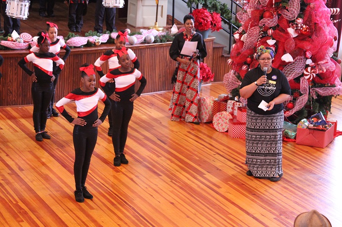 girlsindanceuniformsandwomenstandingbychristmastreewithredbowsandwomanspeakingintomicrophone