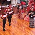 girlsindanceuniformsandwomenstandingbychristmastreewithredbowsandwomanspeakingintomicrophone