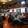 PeoplesittingatcirculartablesinalargeballroomfloorAdditionalseatingseenonthebalconyinsidetheroom