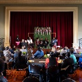 Alargegatheringofpeoplesittingatcirculartableslookingatthestagewhereagroupofwomensitpanel-style