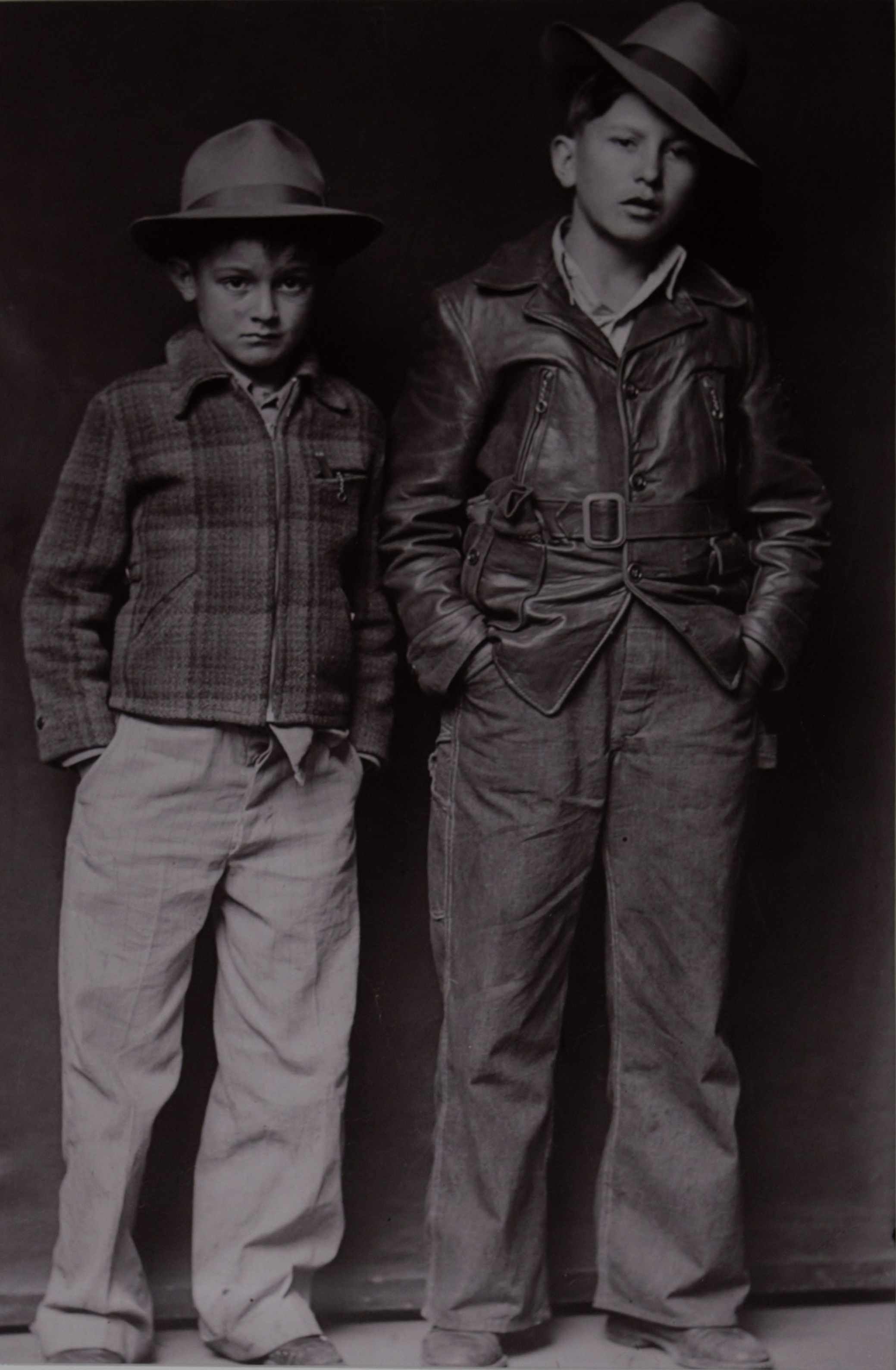 Two young boys stand next to one another posing against a dark backdrop.